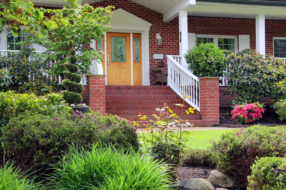 Beautifully and professionally landscaped entrance to a large brick house in a neighborhood.